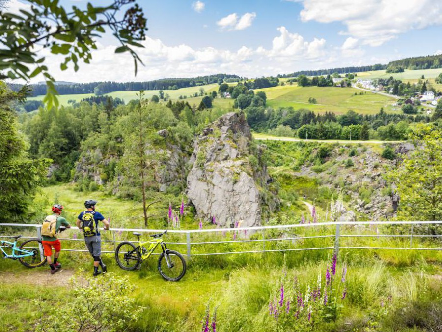 Zwei Radfahrer und ihre Räder machen eine Pause und genießen an einen Weidezaun gelehnt die Landschaft im Erzgebirge.