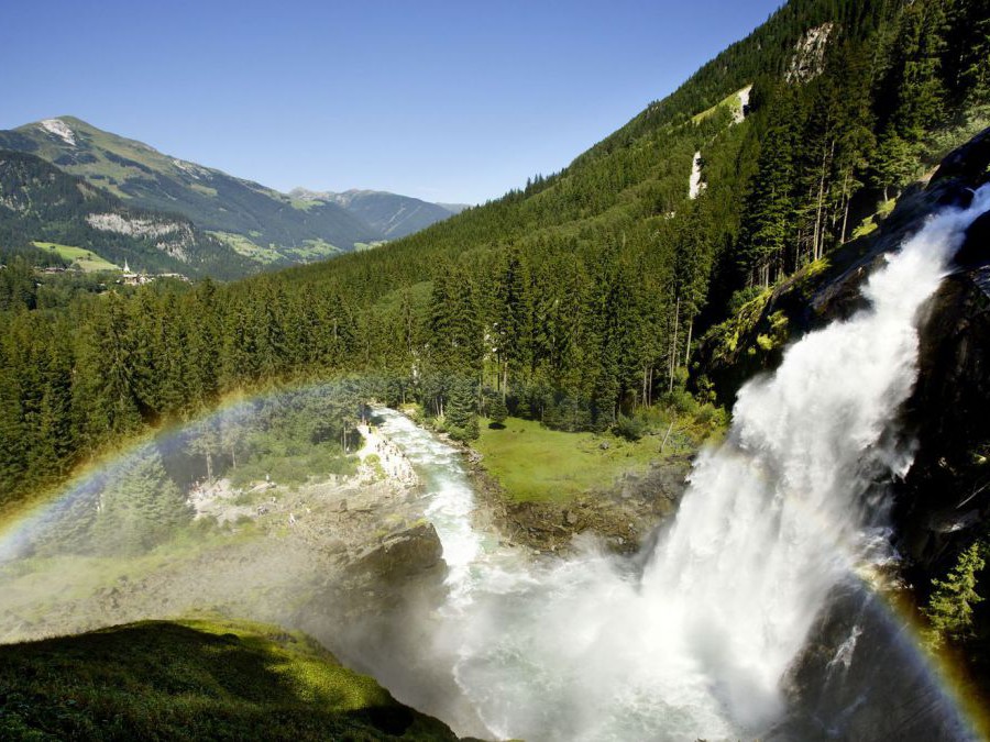 Ein Wasserfall in bewaldeter Berglandschaft, im Sprühnebel des Wasserfalls ist ein Regenbogen sichtbar.