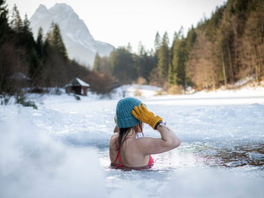 Frau mit Haube in einem Loch in einem zugefrorenen See.