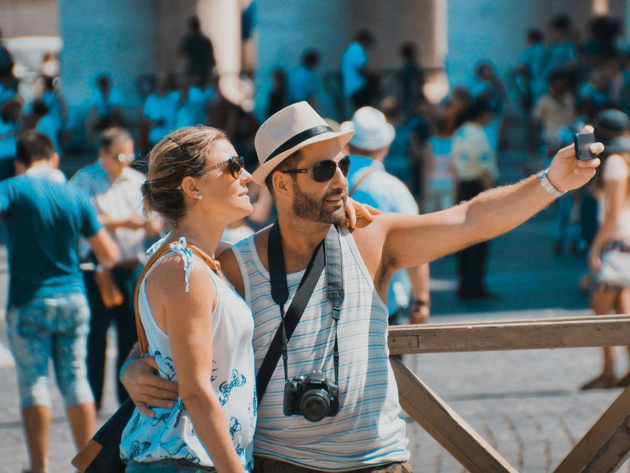 Mann und Frau machen ein Selfie auf einem belebten Platz mit vielen Touristen.