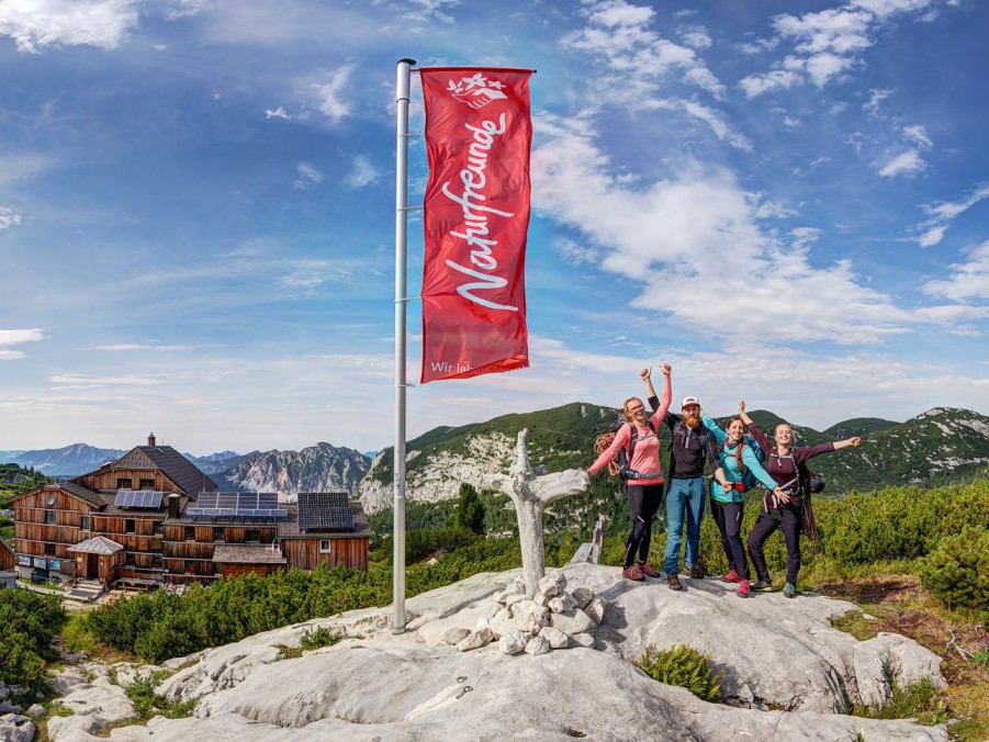 Fahne der naturfreunde und vier Personen auf einem Felsen davor.