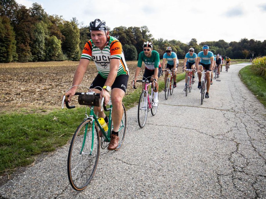 Gruppe von Radfahrern auf einer schmalen asphaltierten Straße.